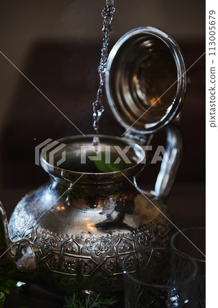 Pouring boiling water into a silver teapot while preparing traditional Moroccan mint tea. Moroccan mint tea Pouring boiling water into a silver teapot while preparing traditional Moroccan mint tea. Moroccan mint tea 113005679