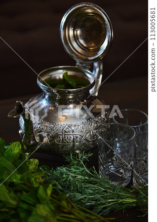 Silver teapot and a bunch of fresh green mint. Traditional Moroccan tea as symbol of the hospitality of Moroccan people Silver teapot and a bunch of fresh green mint. Traditional Moroccan tea as symbol of the hospitality of Moroccan people 113005681