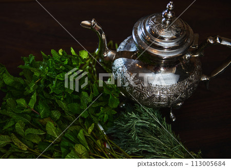 Overhead view Silver teapot and bunch of mint. Traditional Moroccan tea as symbol of the hospitality of Moroccan people Overhead view Silver teapot and bunch of mint. Traditional Moroccan tea as symbol of the hospitality of Moroccan people 113005684