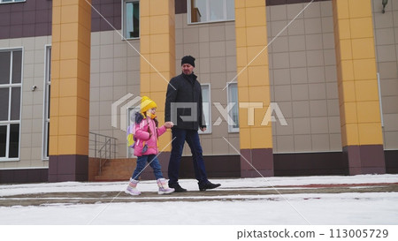 little child with backpack goes school, holding his father hand, caring young father, happy family, cheerful child girl walks with backpack into school building, snowy weather, people outdoors winter 113005729