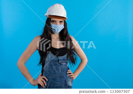 A young woman at a construction site wearing a helmet and a protective mask waits for orders from her superiors. A young woman at a construction site wearing a helmet and a protective mask waits for orders from her superiors. 113007307