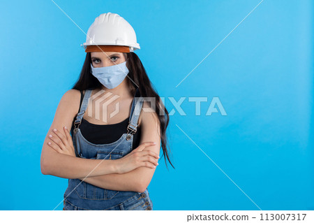 A young woman at a construction site wearing a helmet and a protective mask waits for orders from her superiors. A young woman at a construction site wearing a helmet and a protective mask waits for orders from her superiors. 113007317