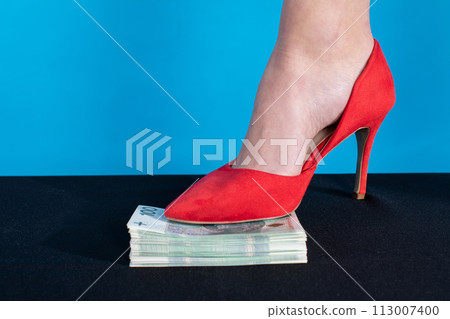 A female foot in a red high heel presses a bundle of money. A female foot in a red high heel presses a bundle of money. 113007400