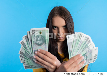 The young woman holds a fan of paper banknotes with a face value of one hundred zlotys. 113007480