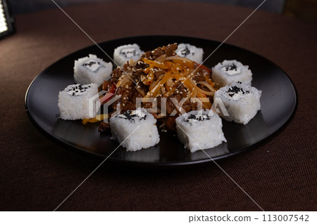 Japanese cuisine, rice rolls with sesame seeds and soy sauce on a black plate Japanese cuisine, rice rolls with sesame seeds and soy sauce on a black plate 113007542