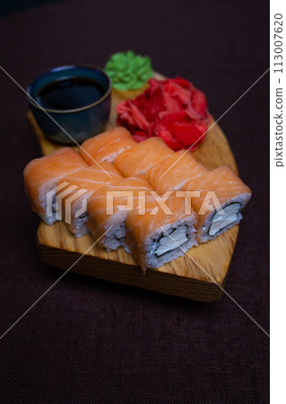 Sushi rolls, wasabi, pickled ginger on wooden plate, dark background 113007620