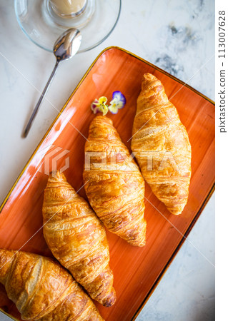 Top view four golden croissants on an orange plate with a cup of coffee on the side Top view four golden croissants on an orange plate with a cup of coffee on the side 113007628