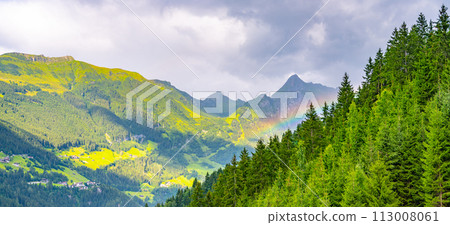 A vibrant rainbow arcs through the mist above a dense, green forest with mountain peaks in the distance. A vibrant rainbow arcs through the mist above a dense, green forest with mountain peaks in the distance. 113008061