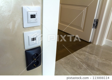 Modern house interior with warm floor controller panels on the wall, wooden parquet and white door Modern house interior with warm floor controller panels on the wall, wooden parquet and white door 113008114