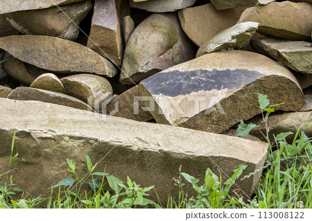 Lit by sun pile of big crackled different sizes and shapes light soft brown stones on green grass. Natural resources, building material, construction and decoration concept. Lit by sun pile of big crackled different sizes and shapes light soft brown stones on green grass. Natural resources, building material, construction and decoration concept. 113008122