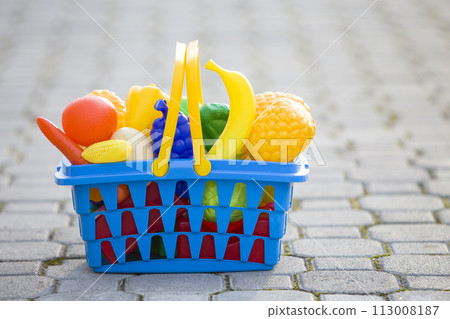 Bright plastic colorful basket with toy fruits and vegetables outdoors on sunny summer day. Bright plastic colorful basket with toy fruits and vegetables outdoors on sunny summer day. 113008187
