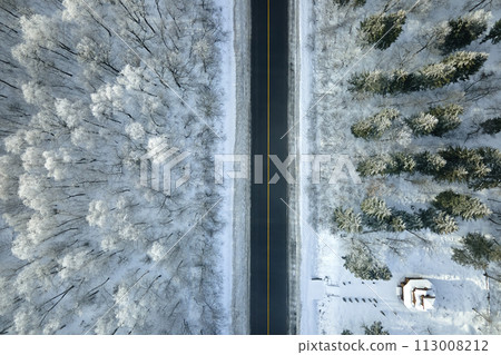 Aerial view of winter landscape with snow covered woods and black asphalt forest road on cold wintry day Aerial view of winter landscape with snow covered woods and black asphalt forest road on cold wintry day 113008212