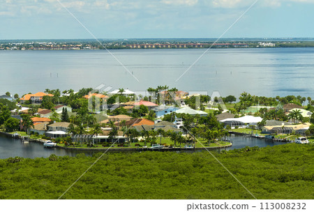 Aerial view of residential suburbs with private homes located near wildlife wetlands with green vegetation on sea shore. Living close to nature concept Aerial view of residential suburbs with private homes located near wildlife wetlands with green vegetation on sea shore. Living close to nature concept 113008232