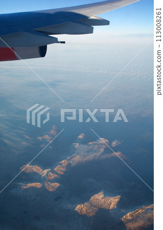 COPENHAGEN, DENMARK - 24 NOV 2018: Aeroplane window view with plane wing flying over the icebergs of Greenland at sunset with aerial perspective 113008261