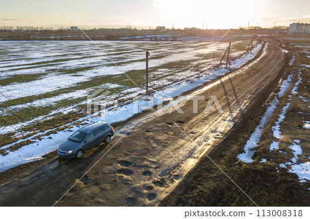 Aerial view of car moving along muddy rural road in bad condition on sunny spring or winter day. 113008318