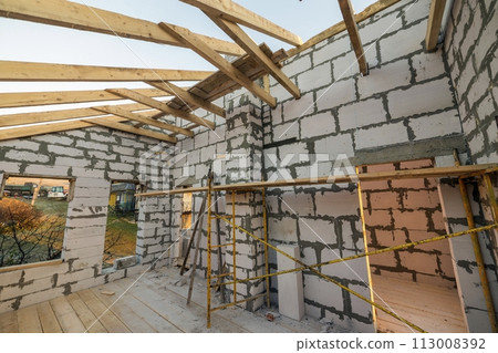 House interior under construction and renovation. Energy saving walls of hollow foam insulation blocks and bricks, ceiling beams and roof frame. 113008392