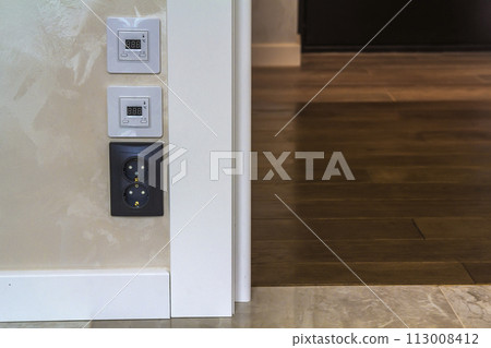Electric socket and warm floor heater control panels on the wall in new renovated room Electric socket and warm floor heater control panels on the wall in new renovated room 113008412