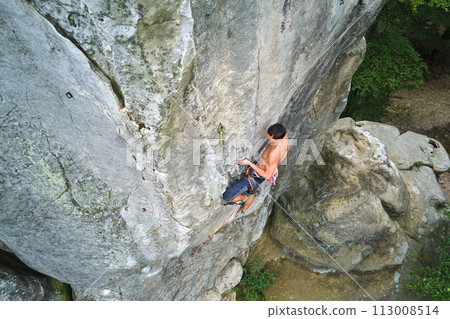 Young man climbing steep wall of rocky mountain. Male climber overcomes challenging route. Engaging in extreme sport concept. 113008514