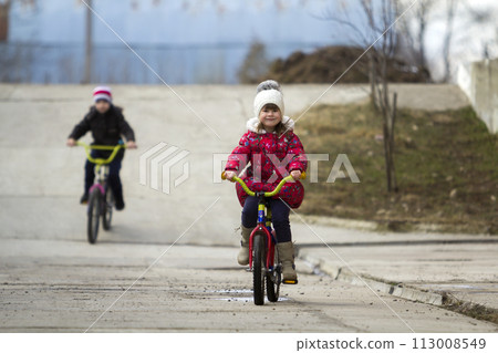 Two happy children boy and girl riding bicycles outdoors in cold weather Two happy children boy and girl riding bicycles outdoors in cold weather 113008549
