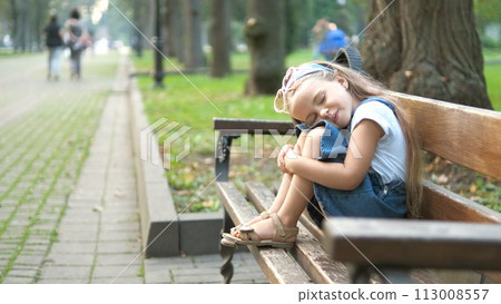 Small tired child girl sitting on a bench with closed eyes resting in summer park. Small tired child girl sitting on a bench with closed eyes resting in summer park. 113008557