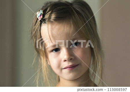 Portrait of little cute pretty young child girl with gray eyes and scattered blond hair smiling shyly in camera on blurred gray background. Beauty, dreams and innocence of childhood concept. 113008597