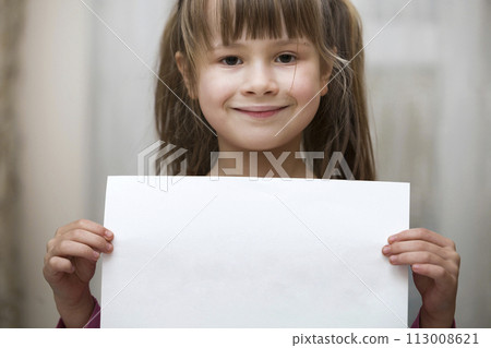 Happy smiling cute child girl holding white copy space sheet of drawing paper. Art education, creativity, advertisement concept. 113008621