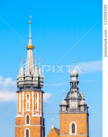 The picturesque towers of Saint Mary Church in Krakow stand tall, showcasing Gothic architecture under a clear blue sky. Krakow, Poland 113008785