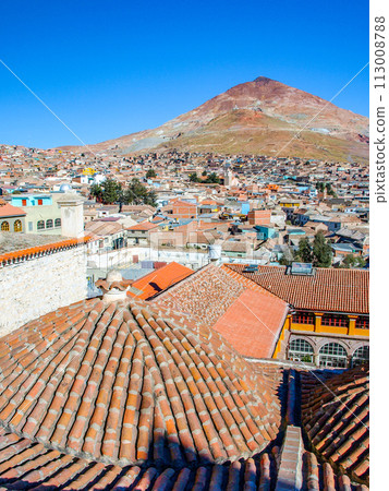 A view of the iconic Cerro Rico mountain looming over the terracotta rooftops of Potosi, Bolivia, on a clear day. 113008788