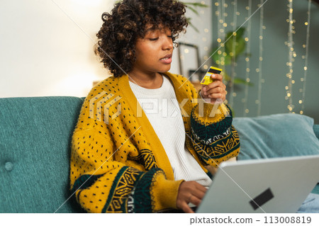 African American woman using laptop shopping online paying with gold credit card. Girl sitting at home buying on Internet enter credit card details. Online shopping ecommerce delivery service African American woman using laptop shopping online paying with gold credit card. Girl sitting at home buying on Internet enter credit card details. Online shopping ecommerce delivery service 113008819