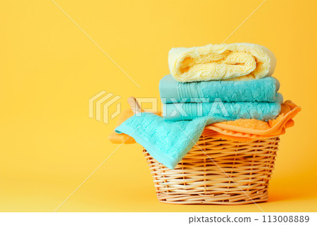 Stack of clean towels in laundry wicker basket on yellow background. The towels showcasing soft and fluffy textures Stack of clean towels in laundry wicker basket on yellow background. The towels showcasing soft and fluffy textures 113008889