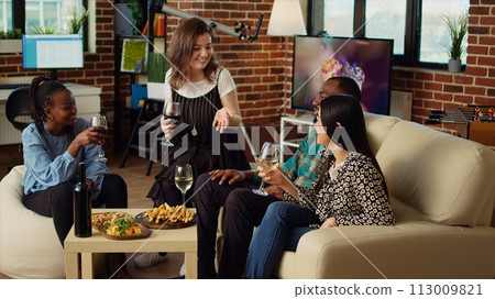 Caucasian woman telling entertaining story to african american and asian friends at apartment party during weekend gathering. Diverse group of people listening to funny tale from host in living room 113009821