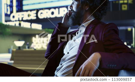 Financial advisor on phone call with accountant at night, sitting on a bench in front of skyscraper office building in the city center. Confident investor trying to obtain new funds from partners. 113009857