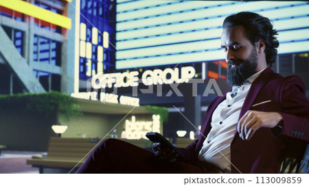 Businessman in suit reading briefing plan for new revenue growth, working on financial management from a bench in the city center. Workaholic billionaire investing global funds under night lights. 113009859