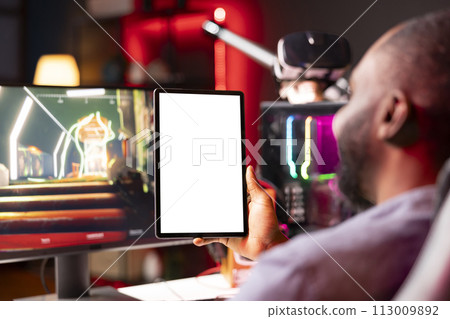 Isolated screen tablet held by gamer competing in online multiplayer videogame at home. Mockup portable device utilized by man playing on gaming PC in neon illuminated apartment 113009892