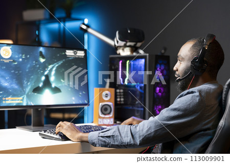 Gamer plays online multiplayer spaceship videogame with friends, relaxing. Player talking with teammates, flying spacecraft, enjoying leisure time in neon lights adorn living room 113009901