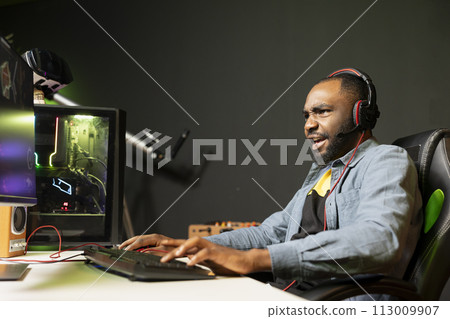 Excited man playing intense videogame on gaming PC at computer desk, enjoying day off, having fun. Focused gamer battling enemies in online multiplayer shooter, feeling strong emotions 113009907