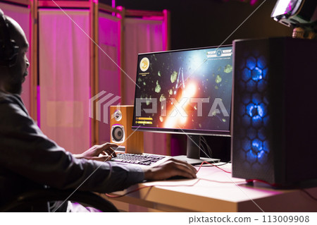 BIPOC person using headphones to enjoy online multiplayer spaceship videogame with friends, shooting asteroids. Player discussing with teammates through headset microphone, flying in galaxy 113009908