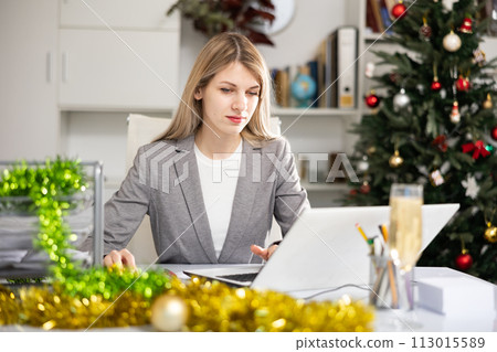 Woman office worker using laptop during Christmastime Woman office worker using laptop during Christmastime 113015589