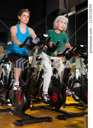 Women exercising on stationary bikes at gym Women exercising on stationary bikes at gym 113015644