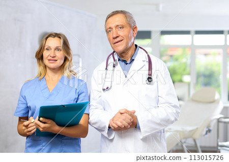 Elderly male doctor with female assistant standing in medical office Elderly male doctor with female assistant standing in medical office 113015726