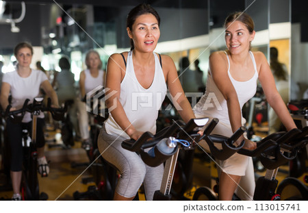 Women training on stationary bikes at gym Women training on stationary bikes at gym 113015741