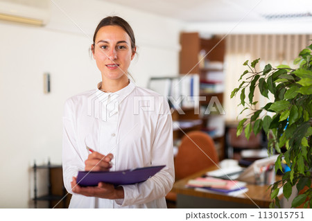 Portrait of a young female manager standing in a office and making notes 113015751