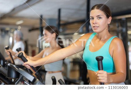 Young woman working out on elliptical machine 113016003