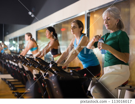 Mature woman with bottle of water after training on bike 113016017