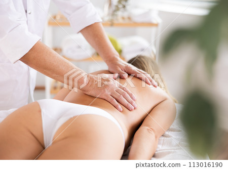 Hands of old masseur conducting back massage for woman client 113016190