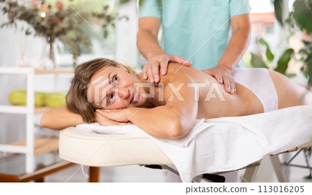 Relaxed middle-aged woman having back massage therapy conducted by skilled masseur Relaxed middle-aged woman having back massage therapy conducted by skilled masseur 113016205