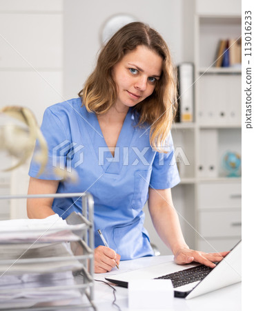 Portrait of female doctor who is working with laptop and documents 113016233