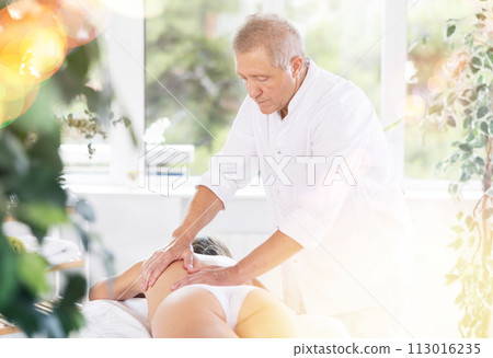 Skilled old masseur conducting back massage for woman client 113016235