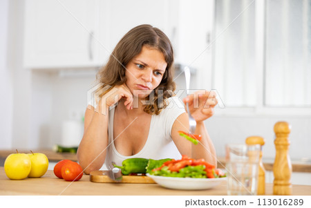 Sad woman eating vegetable salad in kitchen 113016289