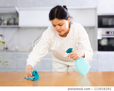 Positive young woman cleaning kitchen table at home 113016291